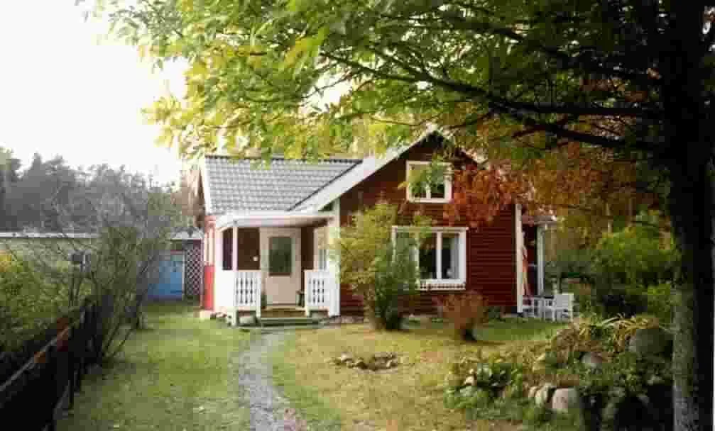 Das rote Holzhaus mit weißen Fensterrahmen im Garten unter Bäumen